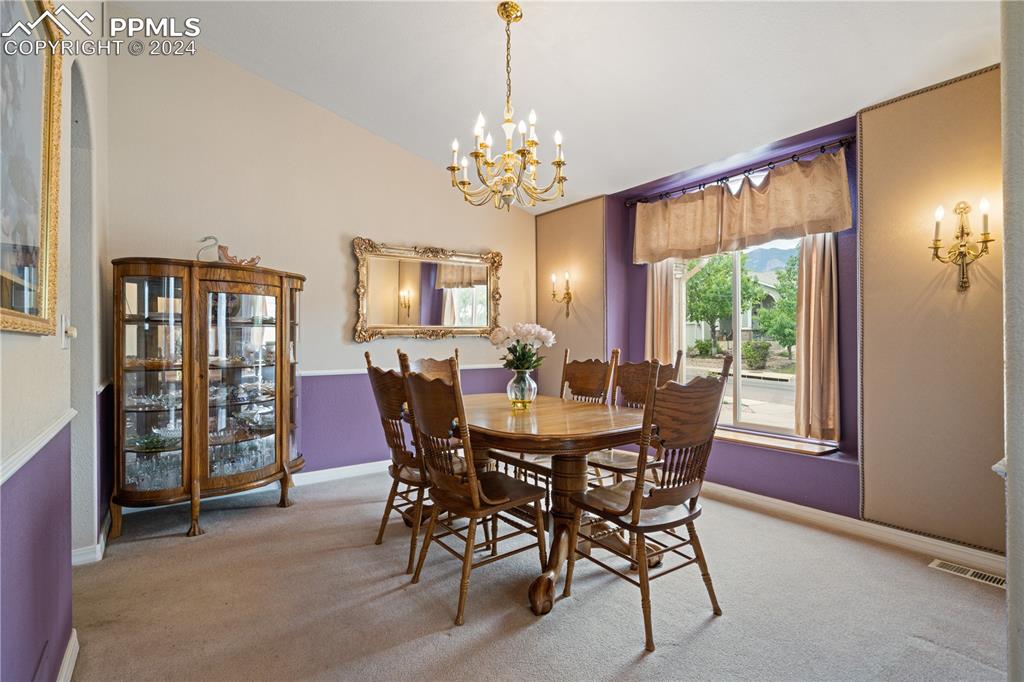 Image 12 of 49: Carpeted dining space with lofted ceiling and an inviting chandelier