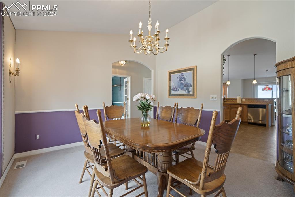 Image 13 of 49: Dining room with high vaulted ceiling, an inviting chandelier, and carpet f