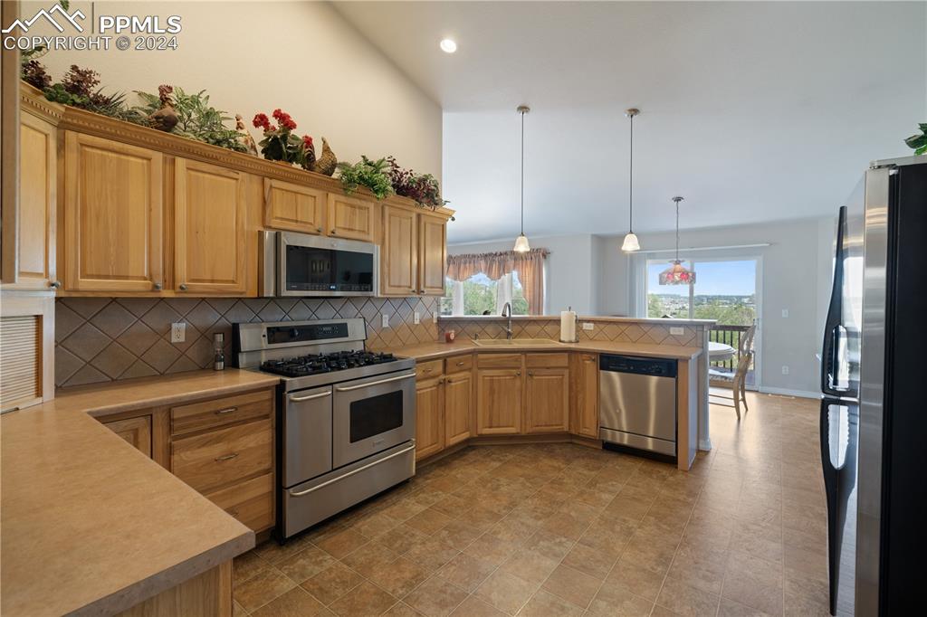 Image 6 of 49: Kitchen with tasteful backsplash, decorative light fixtures, kitchen penins