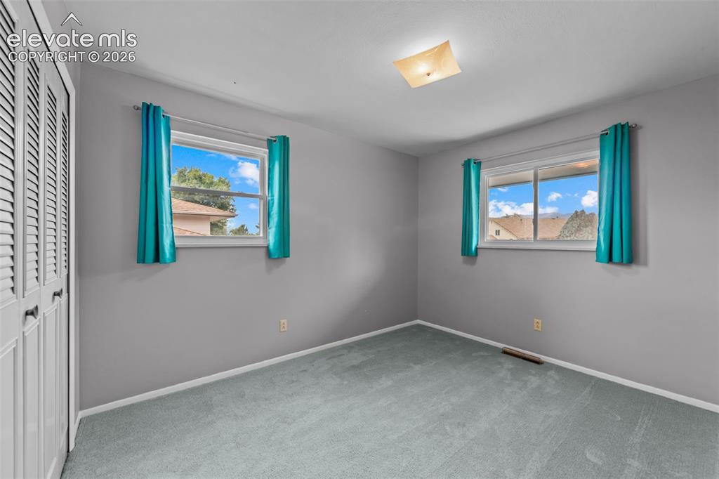 Image 13 of 35: Louvered closet doors, wall-to-wall carpeting, and two windows providing na