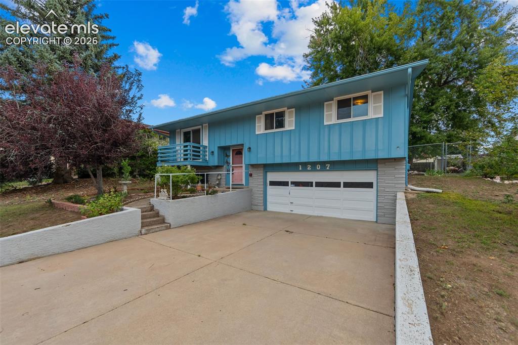 Image 2 of 35: Bi-level residence featuring blue siding, white garage door, and a concrete