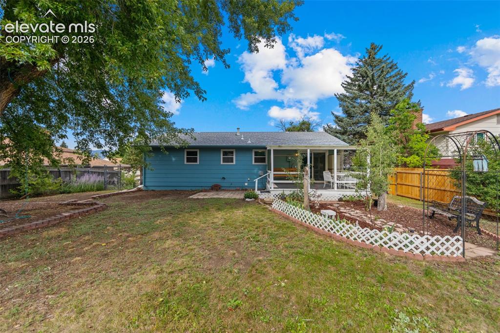 Image 21 of 35: Expansive backyard with a covered deck, tiered landscaping beds, mature tre