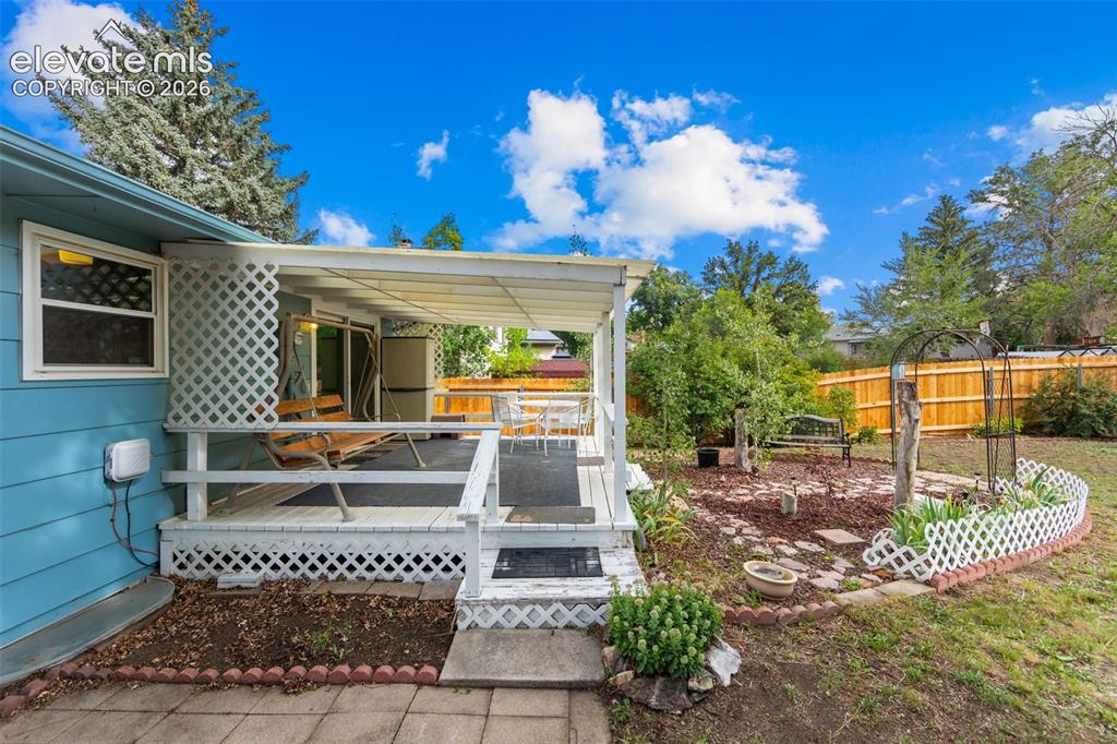 Image 23 of 35: Covered deck with white lattice railing, wood deck surface, and direct yard
