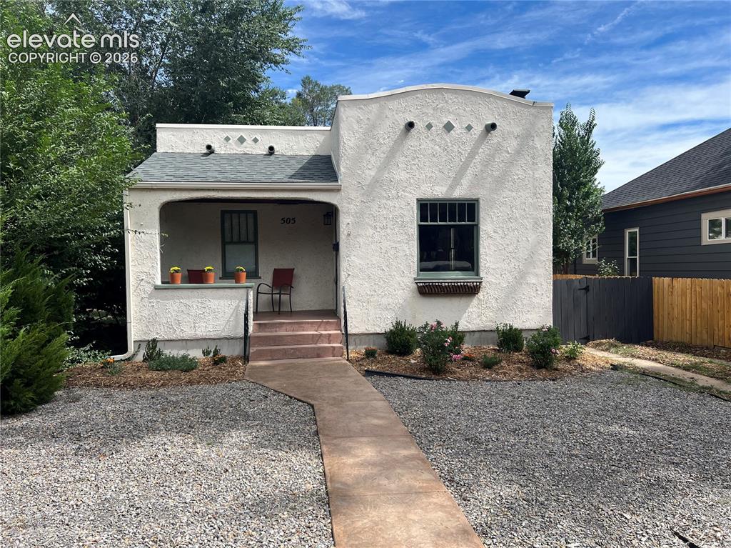 Caption: Main House - Stucco exterior with a covered porch, established landscaping, and a xeriscaped front y
