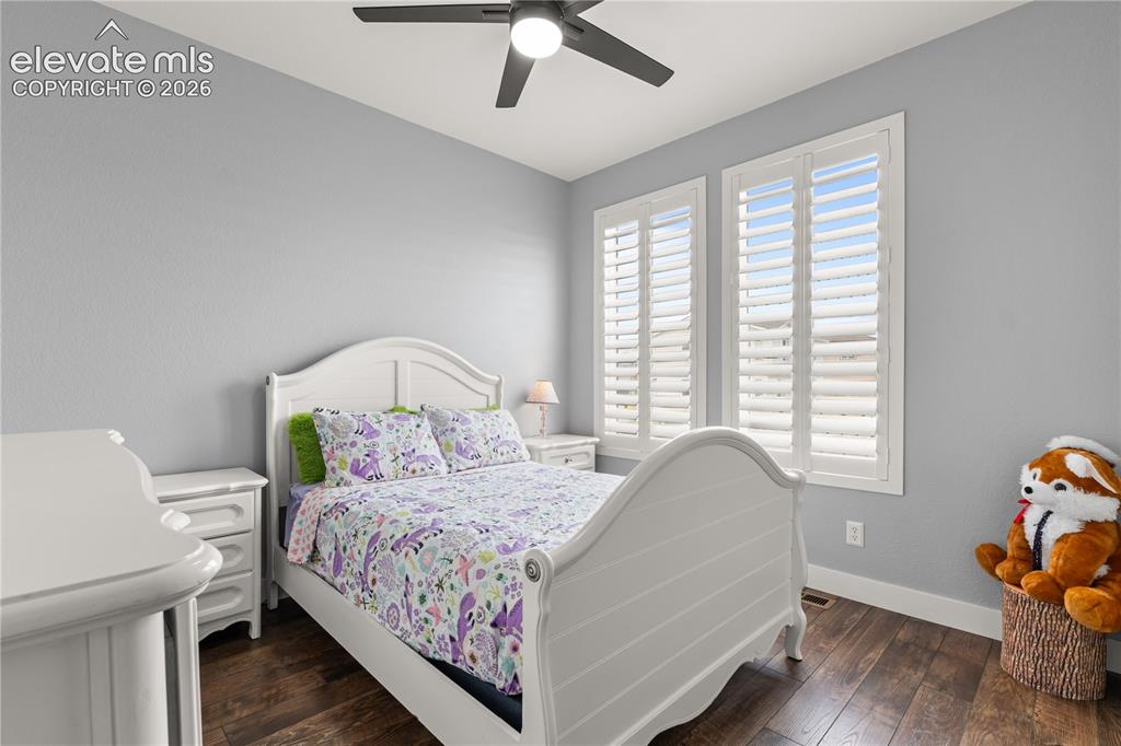 Image 24 of 41: Main level bedroom that is bright with a ceiling fan and plantation shutter