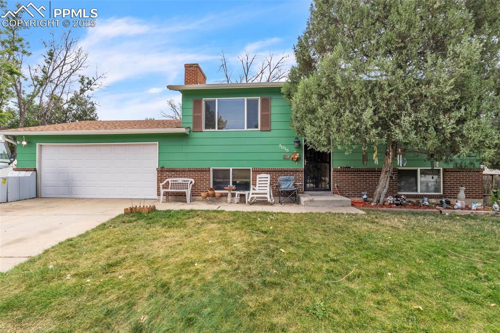 Caption: Bi-level home with brick siding, an attached garage, a front yard, a chimney, and concrete driveway