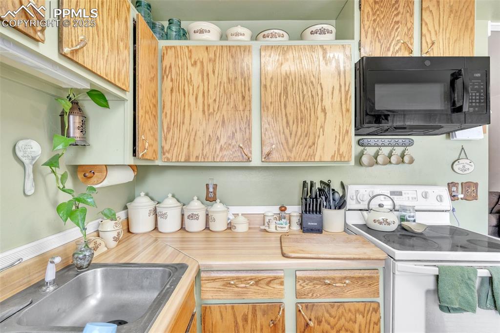 Image 26 of 49: Kitchen with electric range, black microwave, and light countertops