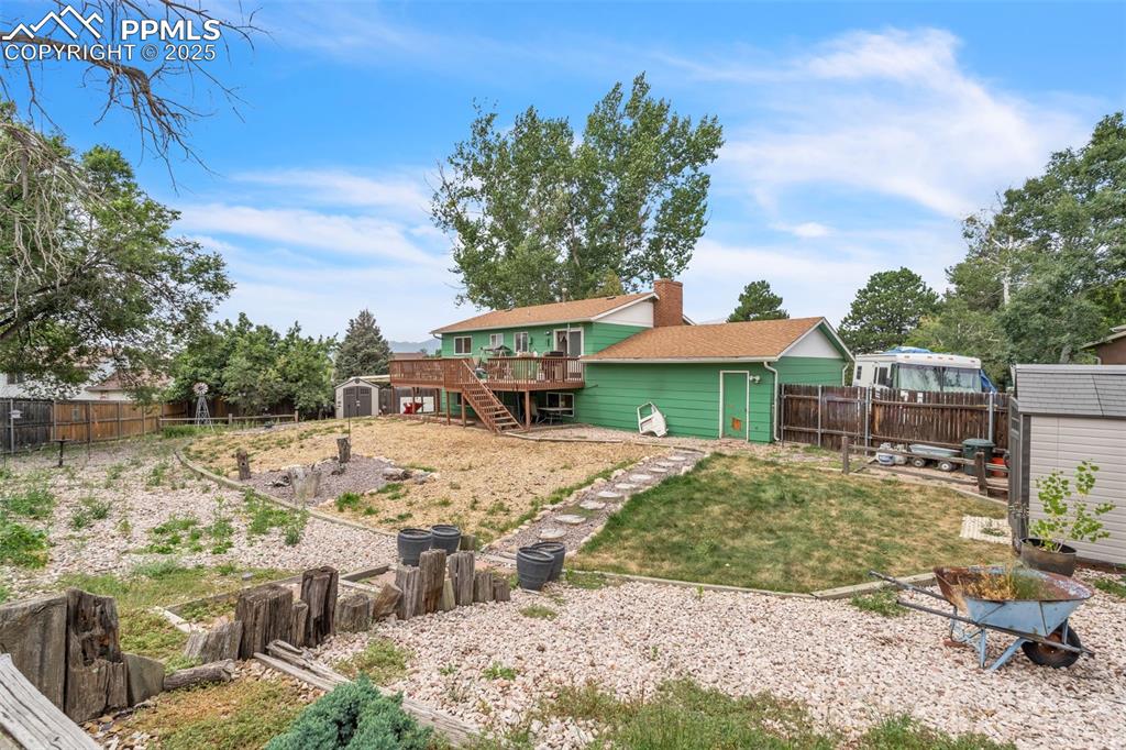 Image 37 of 49: Fenced backyard with a storage unit, stairs, and a deck