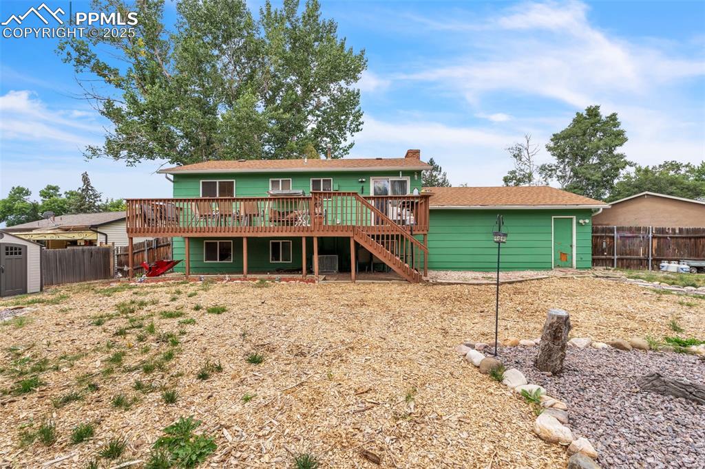 Image 39 of 49: Rear view of house with a storage unit, a deck, stairs, and a chimney