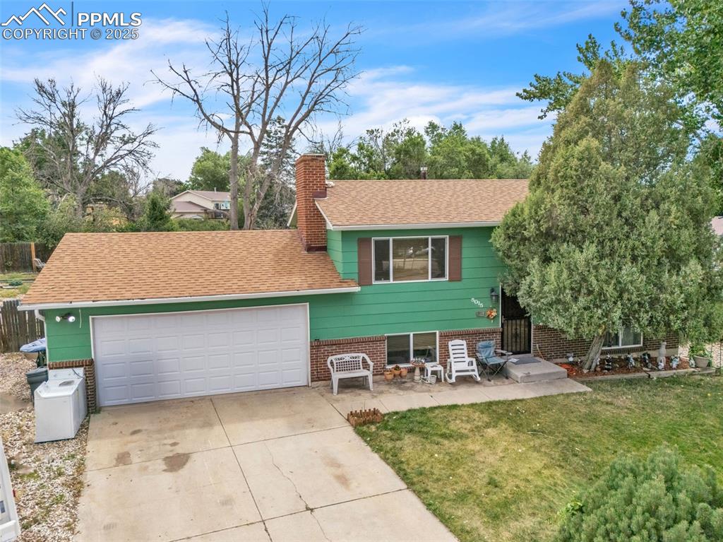 Image 44 of 49: Split level home featuring driveway, a chimney, an attached garage, and bri