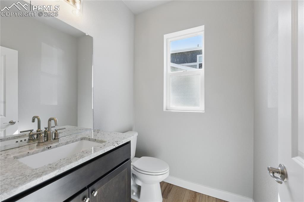 Image 12 of 36: Half bathroom with toilet, vanity, wood finished floors, and baseboards