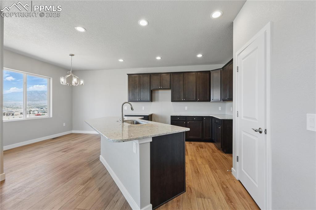 Image 15 of 36: Kitchen with light wood-type flooring, an island with sink, a notable chand