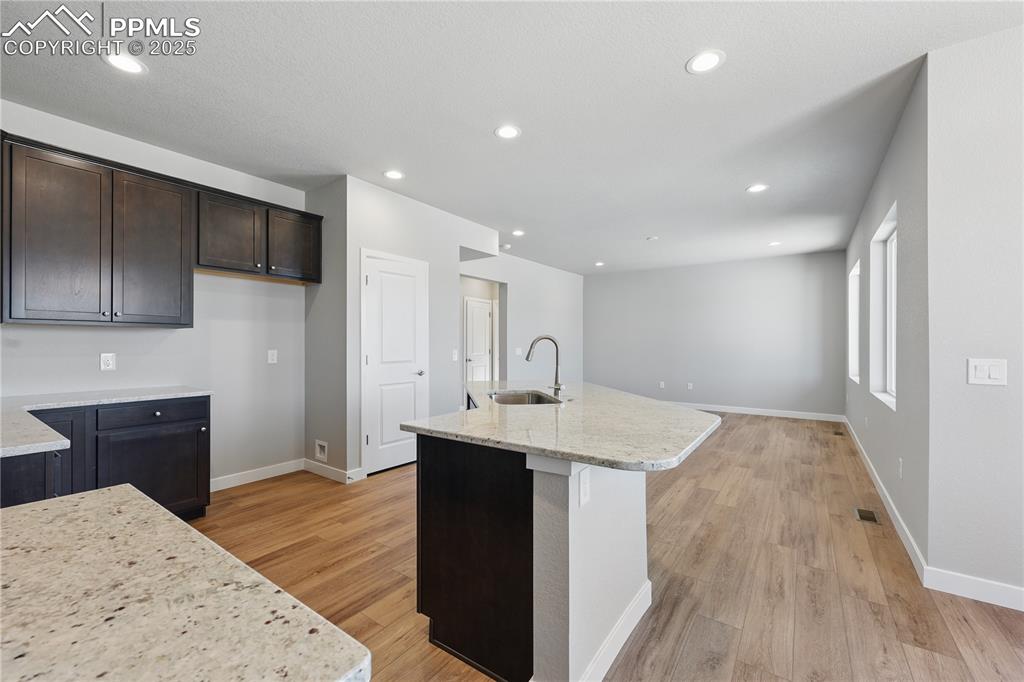 Image 16 of 36: Kitchen with light wood finished floors, a kitchen island with sink, a sink