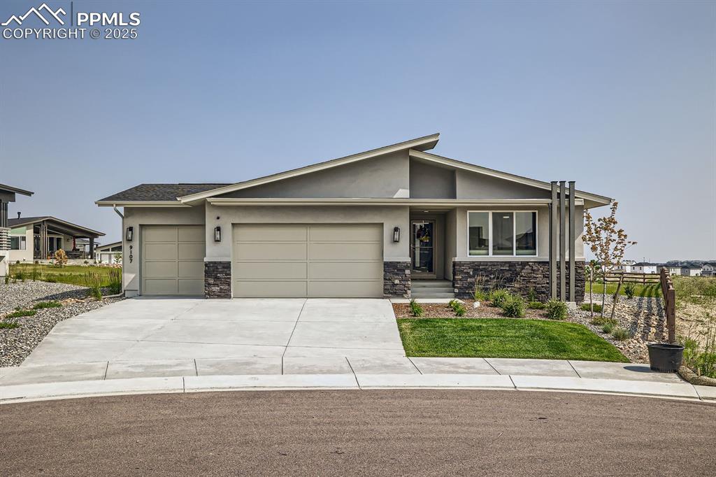 Caption: View of front facade with an attached garage, stone siding, concrete driveway, stucco siding, and co