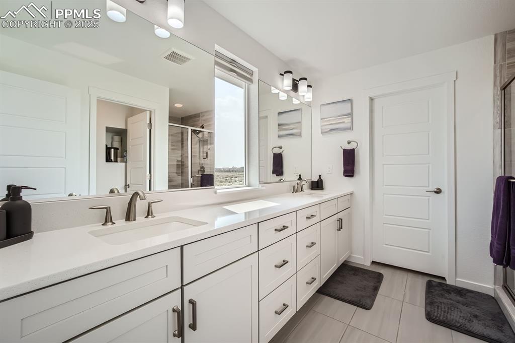 Image 14 of 31: Bathroom with a shower stall, double vanity, and light tile patterned floor