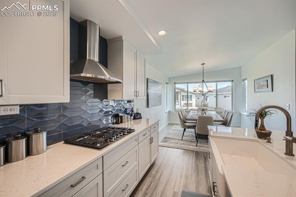 Image 8 of 31: Kitchen with tasteful backsplash, light stone counters, light wood-style fl