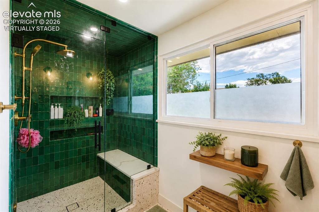 Image 14 of 49: Walk-in shower featuring emerald green subway tile, built-in bench, and gol