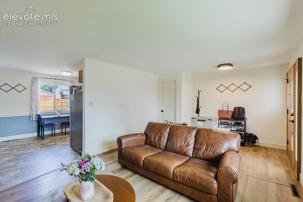 Image 32 of 49: Bright living area with wood-finish flooring, white walls, and a warm-toned
