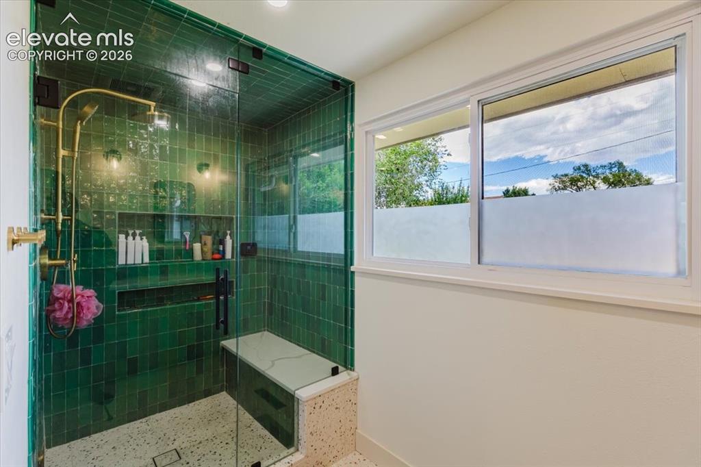 Image 41 of 49: Enclosed shower with emerald green subway tile, built-in shelving, and a br