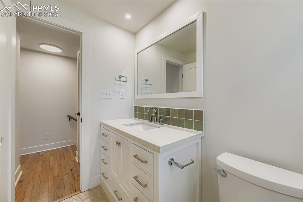 Image 13 of 28: Half bath with decorative backsplash, vanity, and light wood-style flooring