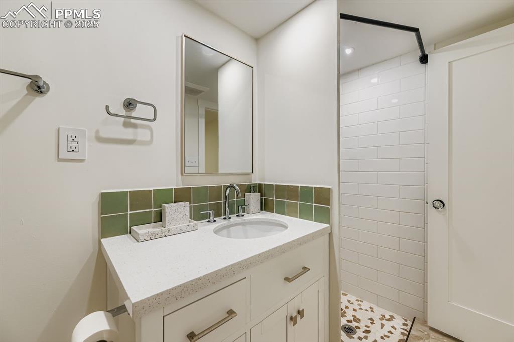 Image 22 of 28: Bathroom with vanity, tiled shower, and tasteful backsplash