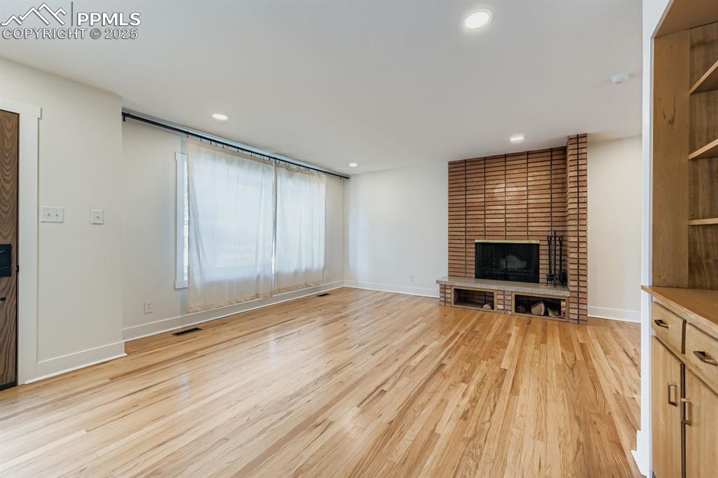 Image 8 of 28: Unfurnished living room with a brick fireplace, light wood-style flooring,
