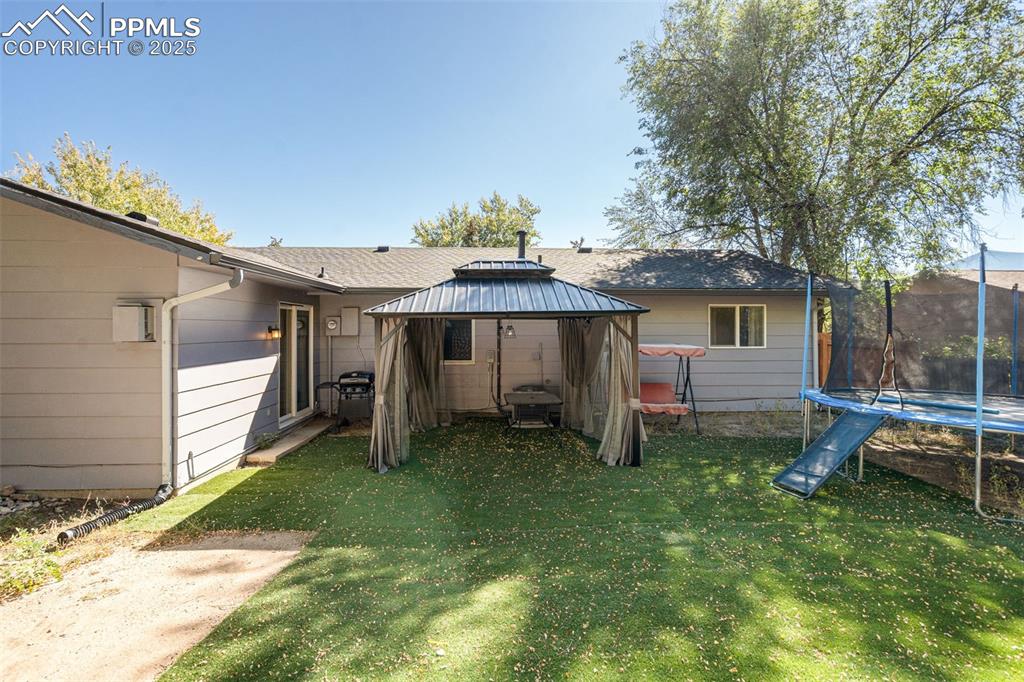 Image 23 of 23: Rear view of house with a trampoline, a gazebo, and a yard