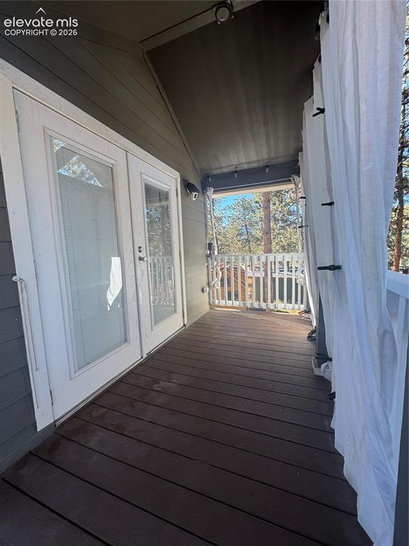 Image 12 of 12: Covered balcony featuring wood-finish decking, white-framed double doors, a
