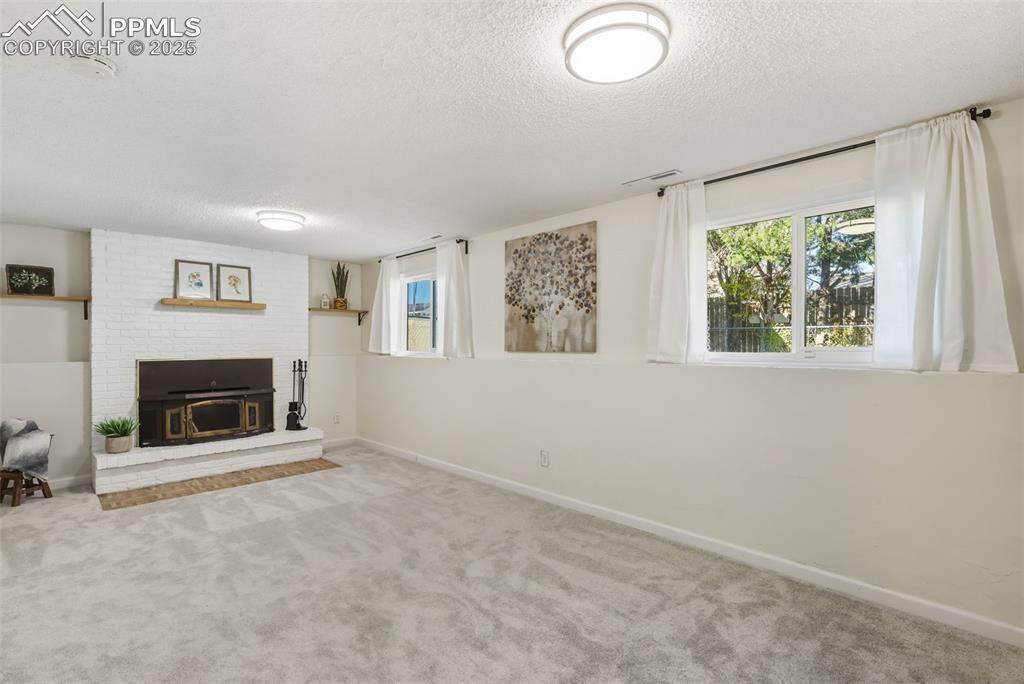 Image 17 of 34: Unfurnished living room with carpet, a textured ceiling, and a brick firepl