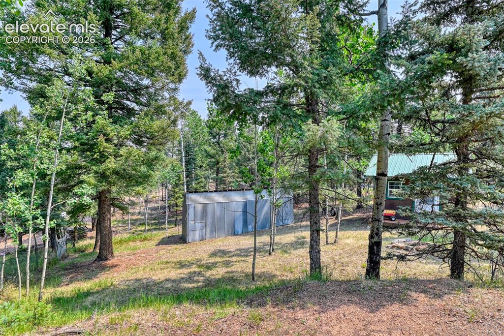 Image 37 of 47: Wooded property with a double sized, metal storage shed at the back of the