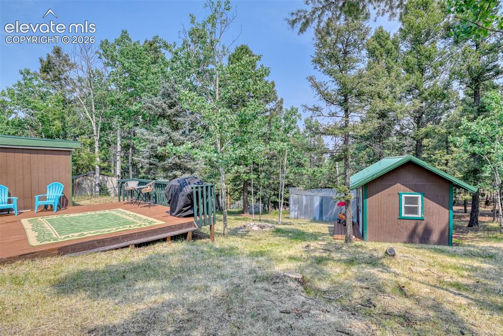 Image 38 of 47: Expansive wooden deck surrounded by mature trees, featuring a guest cabin