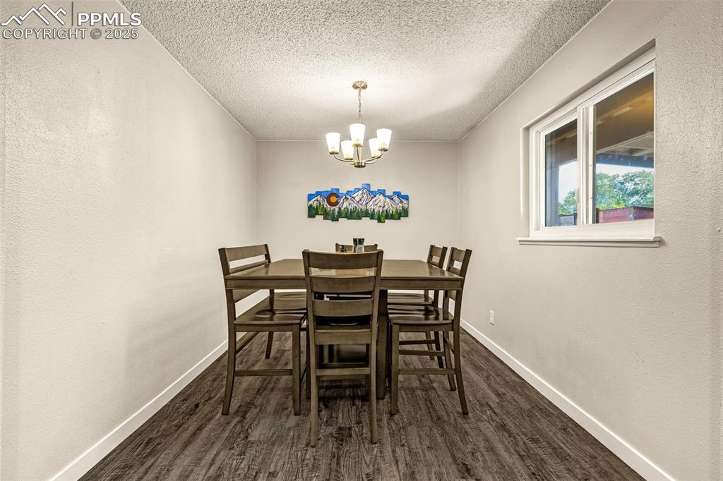 Image 10 of 37: Dining space with dark wood-style floors, a textured wall, a chandelier, an
