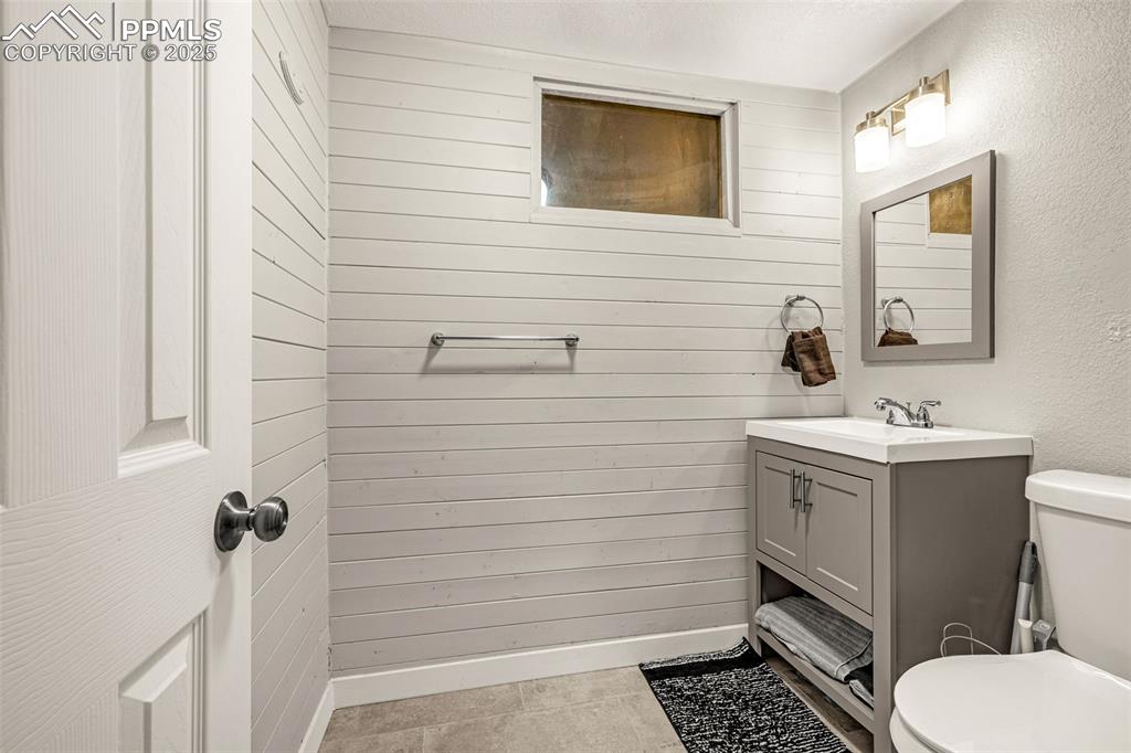 Image 20 of 37: Half bath featuring wood walls, vanity, a textured wall, and light tile pat