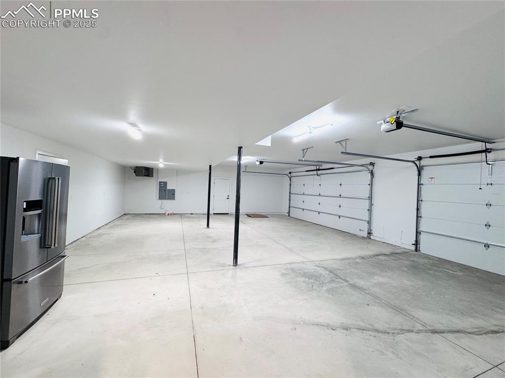 Image 5 of 26: Garage with stainless steel refrigerator with ice dispenser, a garage door 