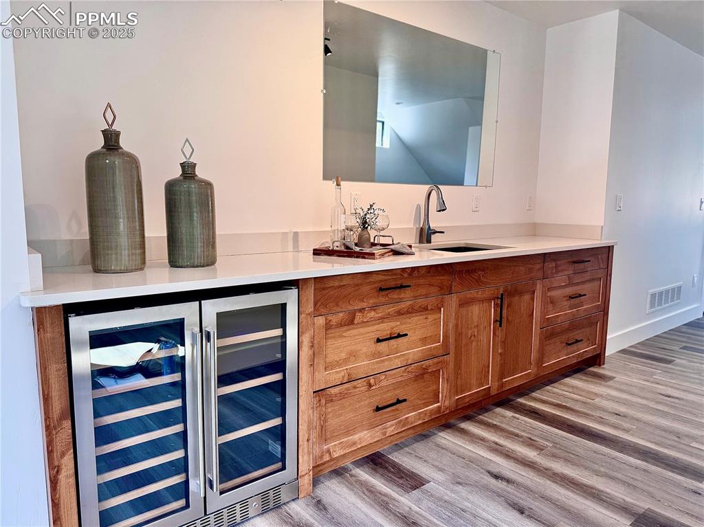 Image 8 of 26: Indoor wet bar featuring beverage cooler and light wood finished floors