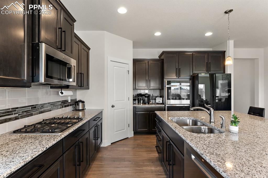 Image 15 of 46: Kitchen featuring dark wood-style floors, light stone counters, a sink, dar