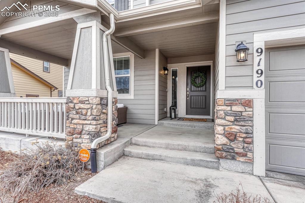 Image 2 of 44: Doorway to property featuring a porch, a garage, and stone siding