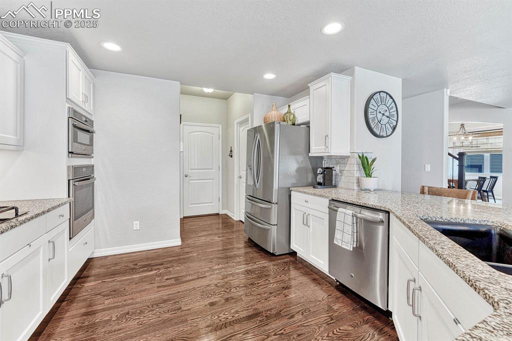 Image 25 of 44: Kitchen with backsplash, white cabinetry, stainless steel appliances, light