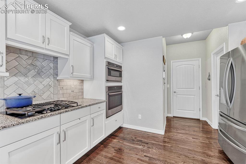 Image 26 of 44: Kitchen featuring dark wood-style floors, stainless steel fridge, white cab
