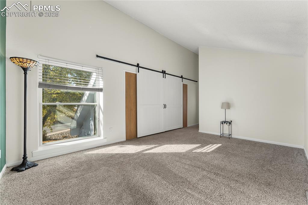 Image 18 of 33: Primary bedroom featuring a barn door, carpet, and high vaulted ceiling