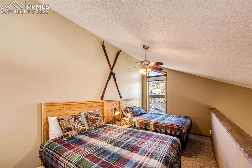 Image 26 of 42: Carpeted bedroom with a textured ceiling, lofted ceiling, and ceiling fan