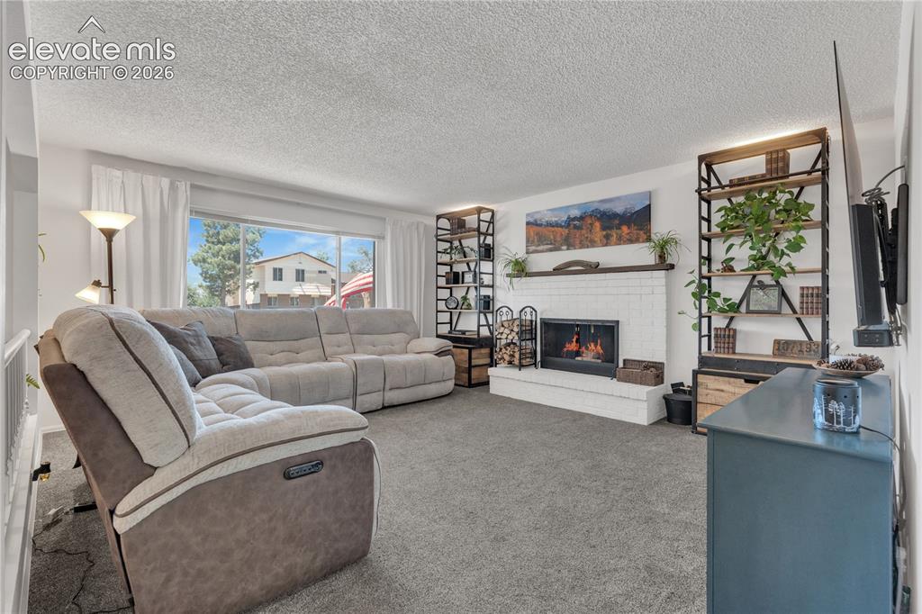 Image 6 of 30: White brick fireplace with a wood mantel, expansive window, and new carpet
