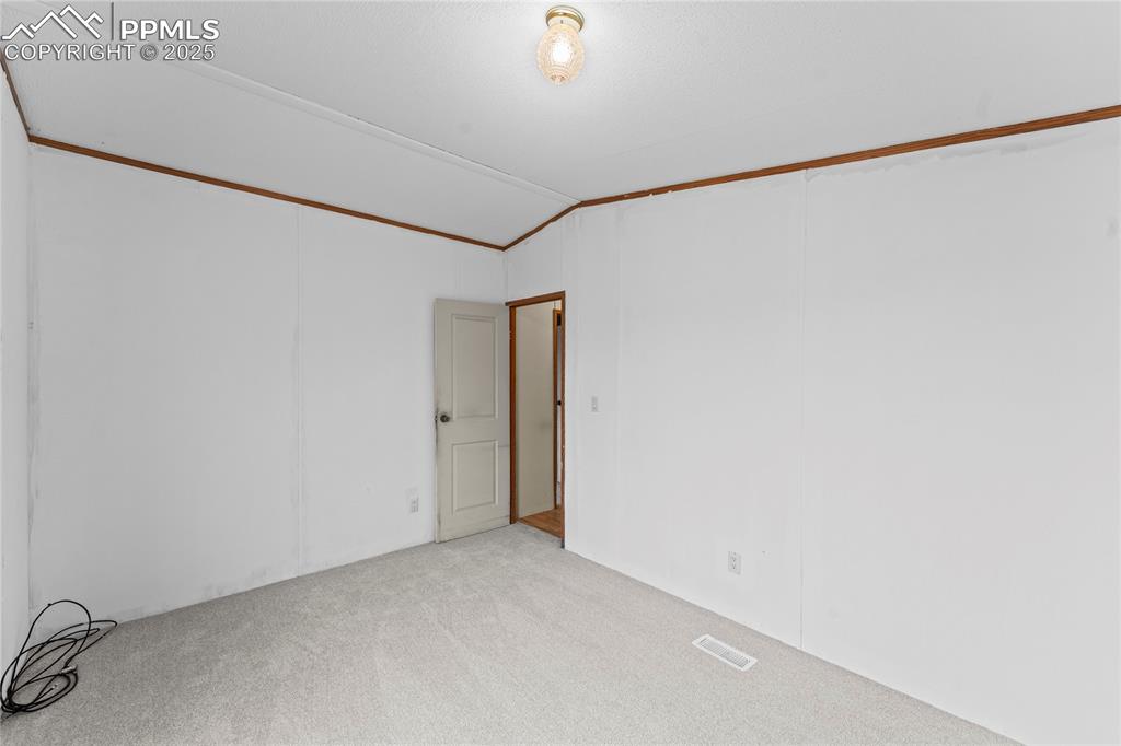 Image 16 of 32: Spare room with vaulted ceiling, carpet flooring, and a decorative wall