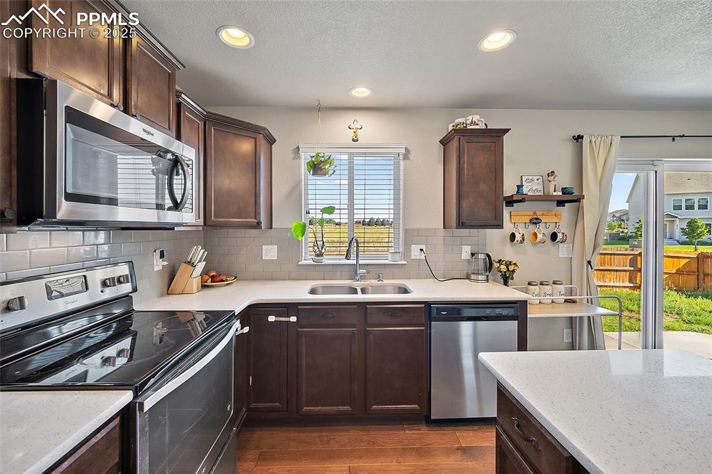 Image 12 of 38: Kitchen featuring stainless steel appliances, dark brown cabinetry, backspl