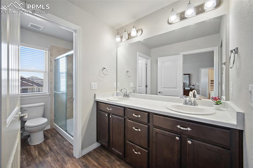 Image 21 of 38: Full bathroom featuring dark wood-type flooring, a shower stall, double van