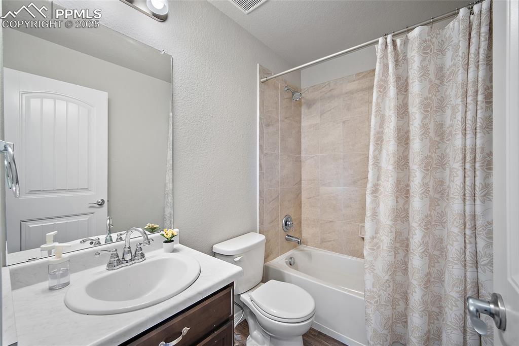 Image 26 of 38: Full bathroom with a textured wall, shower / bathtub combination with curta