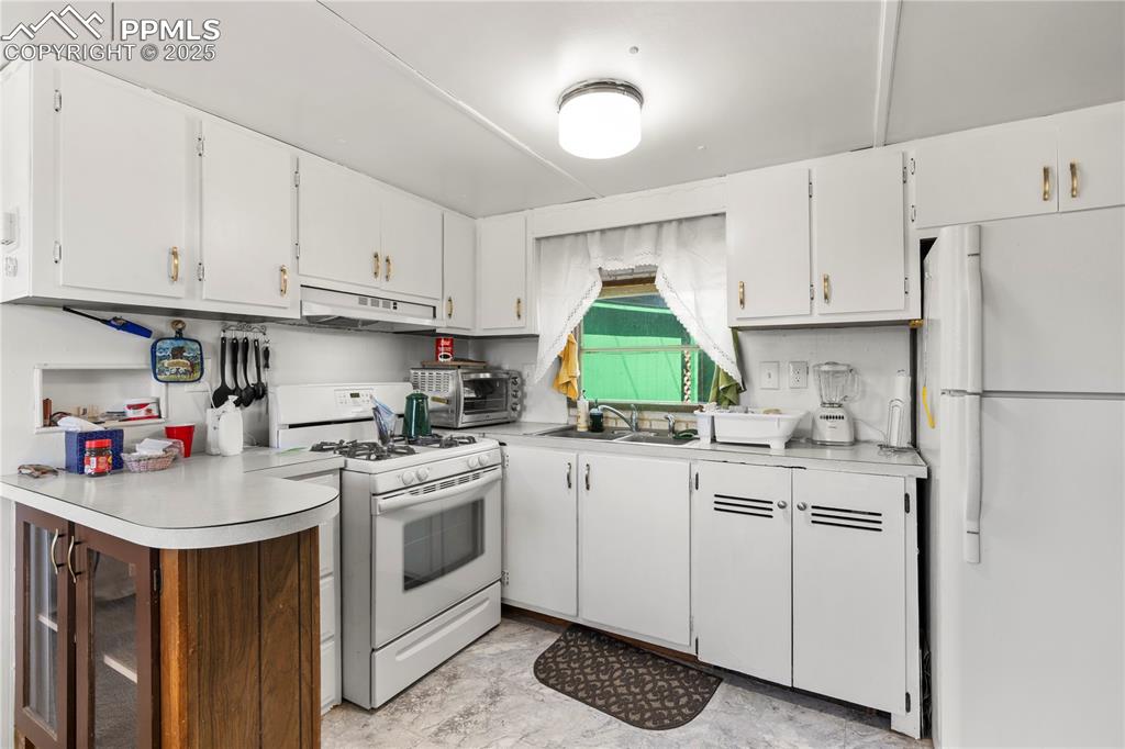 Image 14 of 31: Kitchen with white appliances, white cabinetry, light countertops, and unde