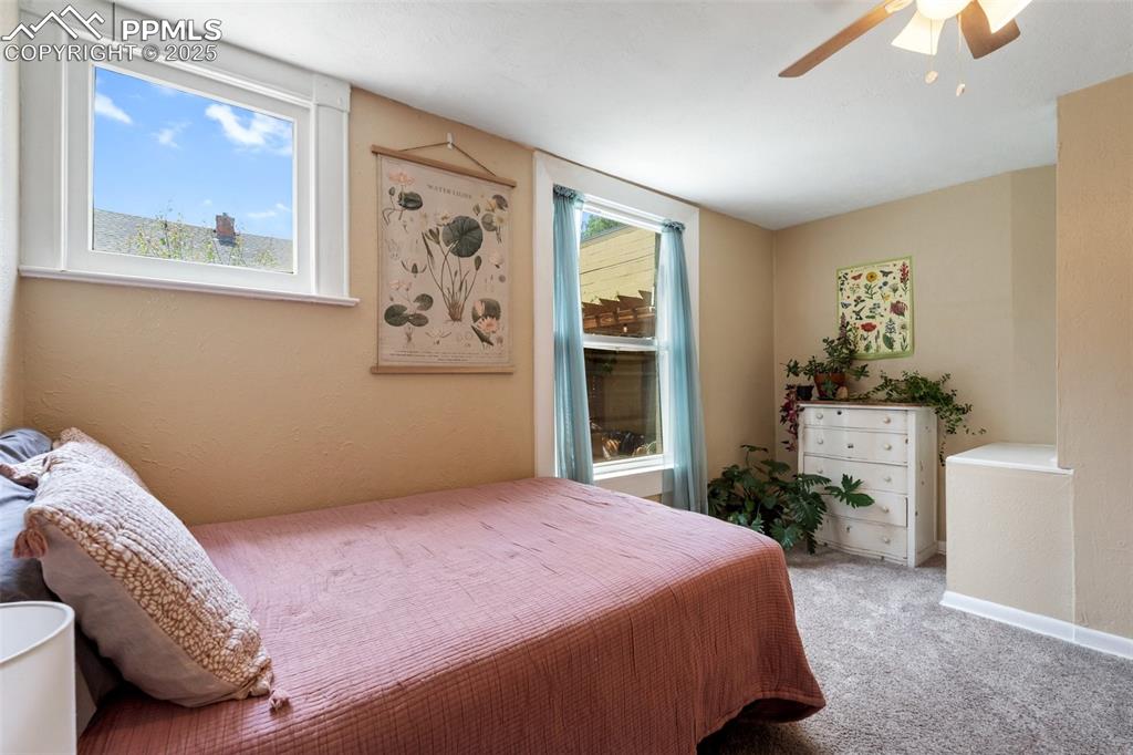 Image 17 of 49: Carpeted bedroom with multiple windows, ceiling fan, and a textured wall