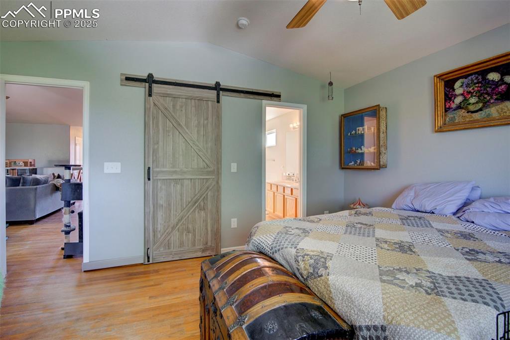 Image 16 of 44: Bedroom with a barn door, light wood-type flooring, lofted ceiling, a ceili