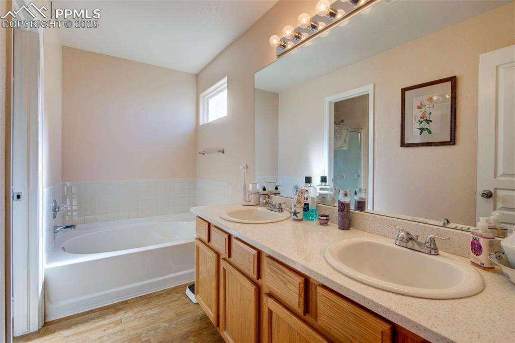 Image 18 of 44: Bathroom featuring double vanity, a bath, and wood finished floors